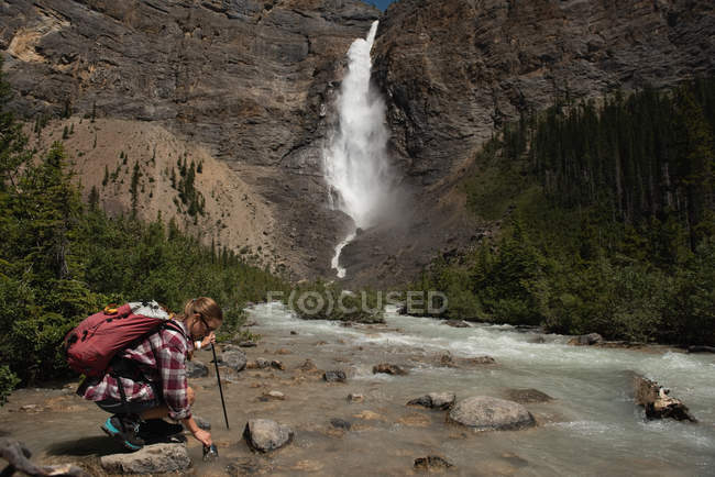 Caminhante feminina enchendo garrafa de água no córrego nas montanhas — Fotografia de Stock