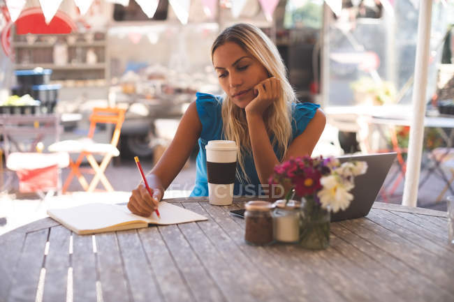 Mujer atenta escribiendo en un libro en la cafetería al aire libre - foto de stock