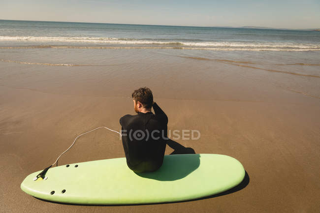 Vue arrière du surfeur assis sur la planche de surf à la plage — Photo de stock