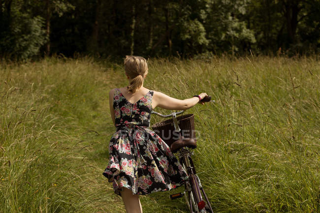 Rückansicht einer Frau, die mit dem Fahrrad im Feld geht — Stockfoto