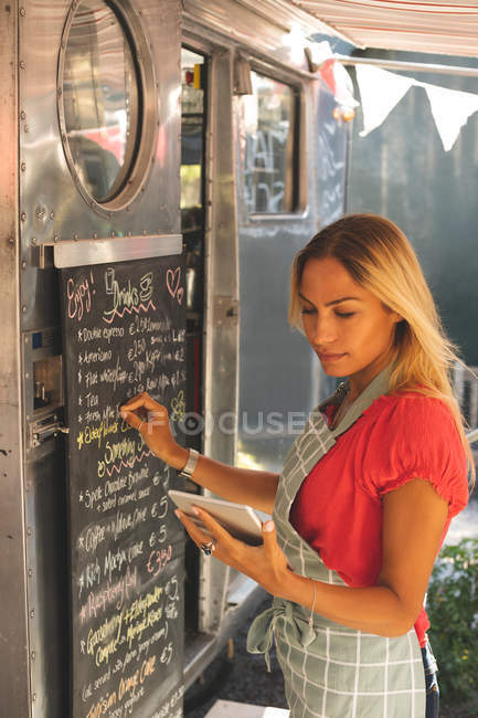 Hermosa camarera femenina menú de escritura en el tablero de menú mientras se utiliza la tableta digital - foto de stock