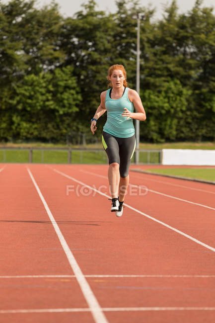 Jeune athlète féminine en course sur piste de sport — Photo de stock