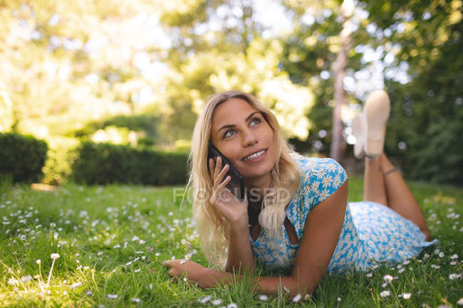 Улыбающаяся женщина разговаривает по мобильному телефону в парке — стоковое фото