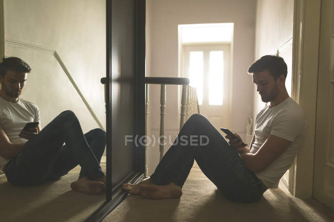 Hombre usando teléfono móvil cerca de escaleras en casa - foto de stock