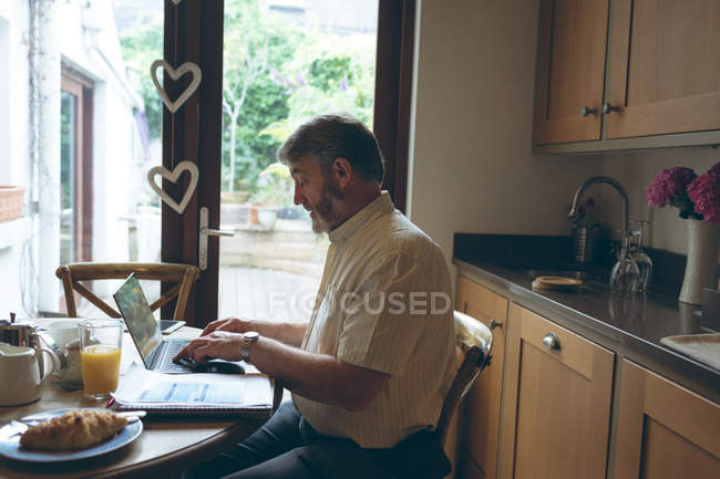 Vue latérale de l'homme âgé utilisant une tablette numérique sur une tablette à manger à la maison — Photo de stock