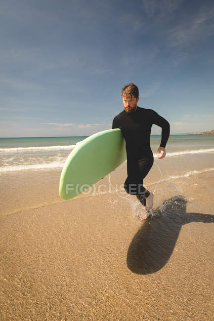 Surfer with surfboard running at beach on a sunny day — Stock Photo