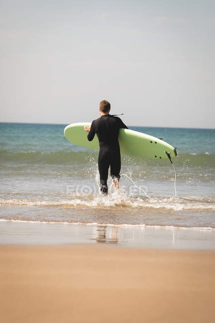 Вид ззаду на серфер з дошкою для серфінгу, що біжить до пляжу — стокове фото