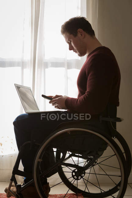 Joven hombre discapacitado usando el teléfono móvil en casa - foto de stock