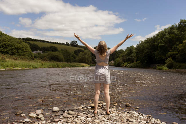 Vue arrière de la femme debout avec les bras près du ruisseau — Photo de stock
