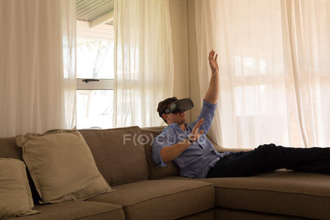 Человек, использующий гарнитуру виртуальной реальности в гостиной дома — стоковое фото