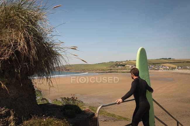 Surfer with surfboard standing on staircase on a sunny day — Stock Photo