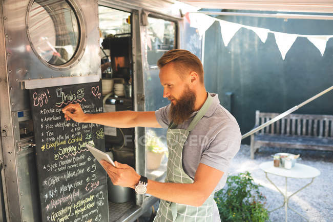 Мужчина официантка пишет меню на доске меню при использовании цифрового планшета — стоковое фото