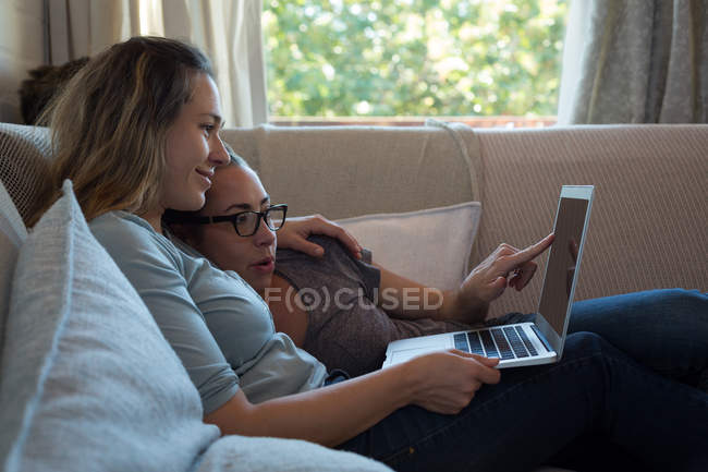 Лесбійська пара використовує ноутбук на дивані вдома. — стокове фото
