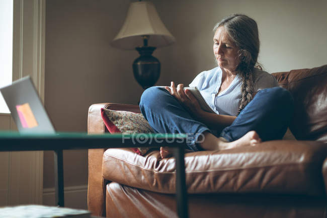 Mujer mayor escribiendo en un bloc de notas en la sala de estar en casa - foto de stock