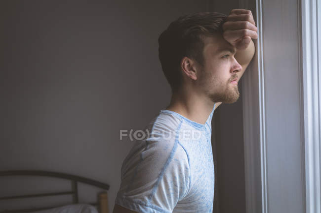 Uomo premuroso che guarda attraverso la finestra a casa — Foto stock
