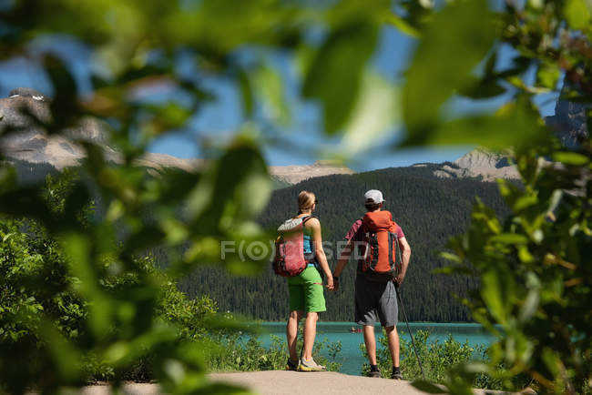 Visão traseira do casal de pé com a mão na mão perto da ribeira — Fotografia de Stock