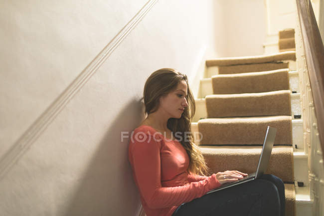 Young woman using laptop on staircase at home — Stock Photo