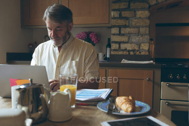 Старший мужчина с помощью цифрового планшета на обеденный планшет дома — стоковое фото