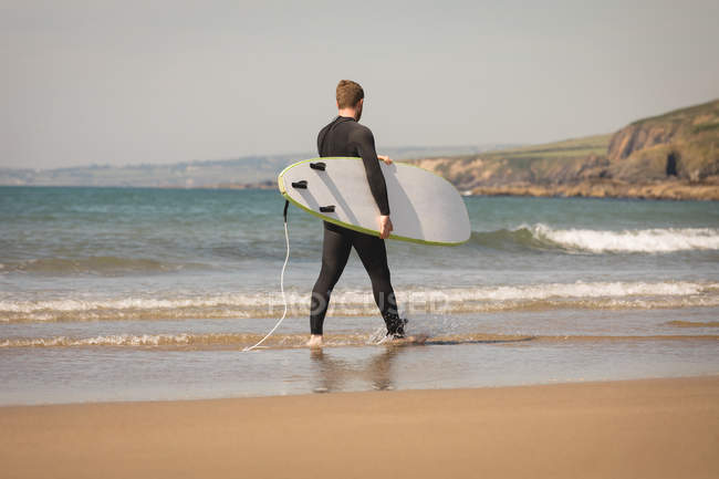 Vista trasera del surfista con tabla de surf caminando en la playa - foto de stock