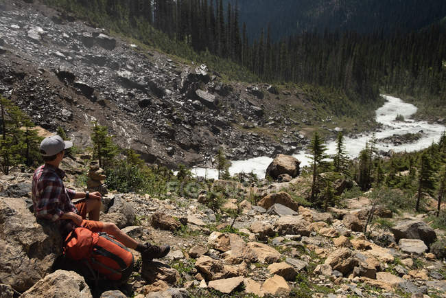 Задуманный турист-мужчина, сидящий на скале в горах — стоковое фото