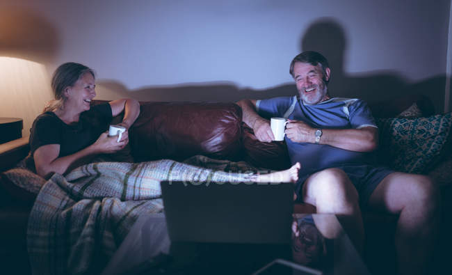Щаслива старша пара дивиться ноутбук, маючи каву вдома — стокове фото