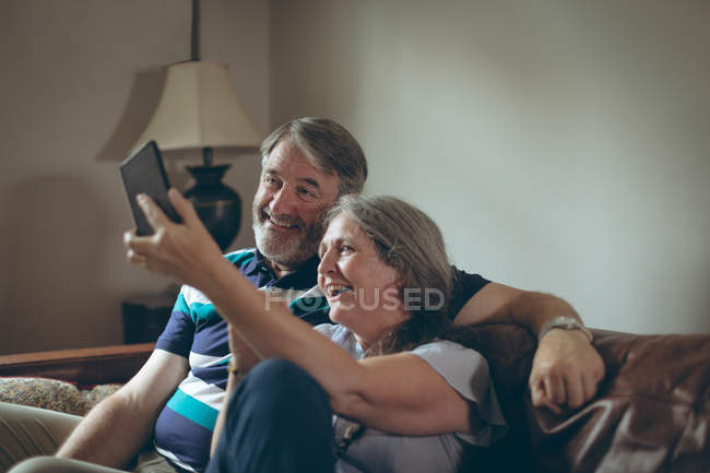 Happy senior couple taking selfie on mobile phone at home — Stock Photo