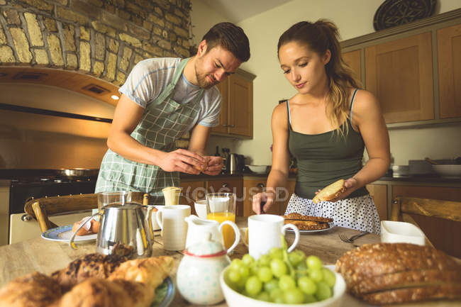 Couple préparant le petit déjeuner sur la table à manger à la maison — Photo de stock