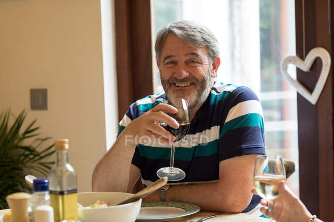 Homem sênior tendo vinho tinto na mesa de jantar em casa — Fotografia de Stock