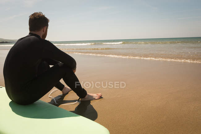 Серфер сидить на дошці на пляжі в сонячний день — стокове фото