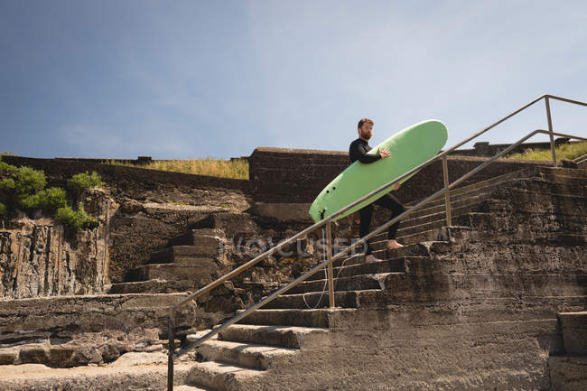 Серфер з дошкою для серфінгу, що йде по сходах біля пляжу — стокове фото