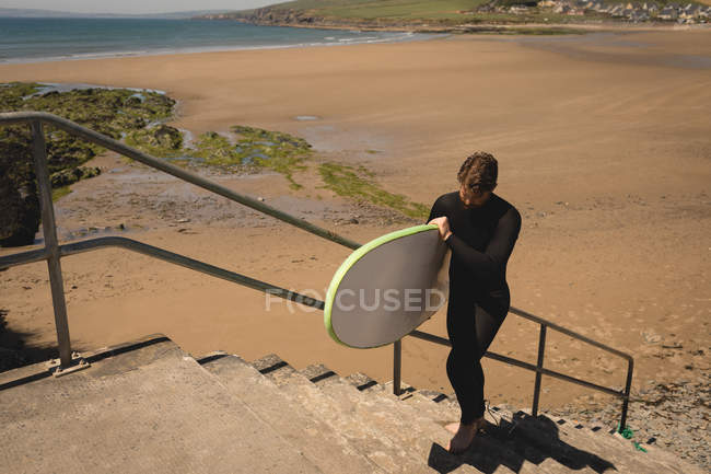 Surfer with surfboard walking on staircase near beach — Stock Photo