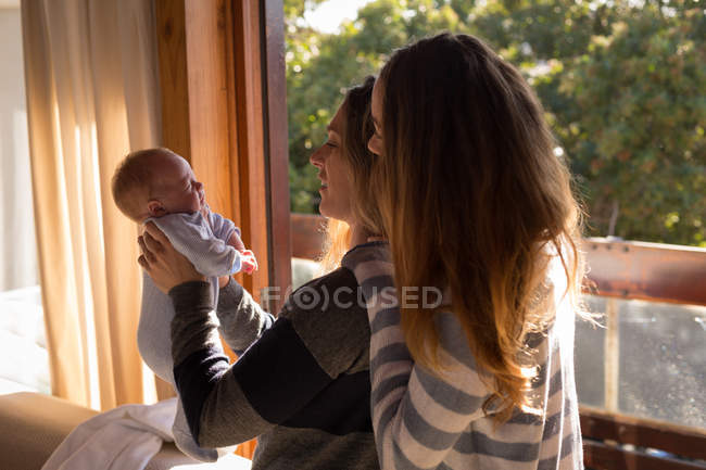 Lesbian couple playing with baby on sofa at home — Stock Photo