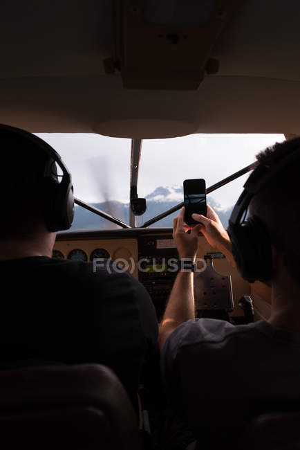 Rückansicht eines Piloten, der Flugzeuge fliegt, während der Co-Pilot Fotos mit dem Handy macht — Stockfoto