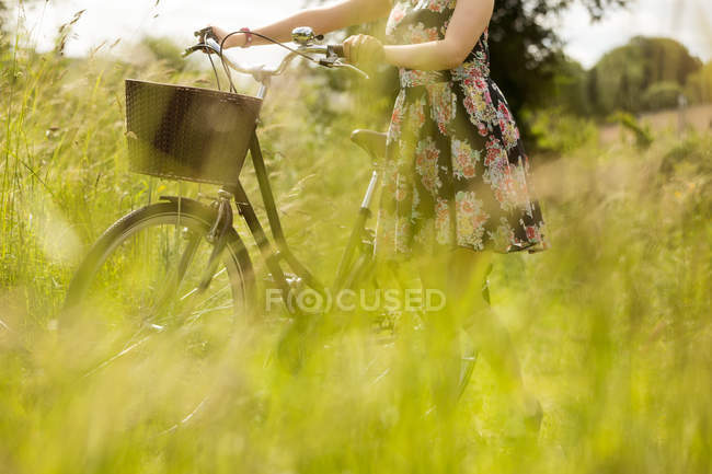 Mittelteil der Frau, die mit dem Fahrrad im Feld geht — Stockfoto