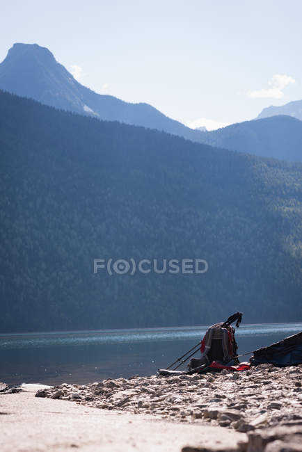 Sac à dos et bâton de randonnée près de la rivière par une journée ensoleillée — Photo de stock
