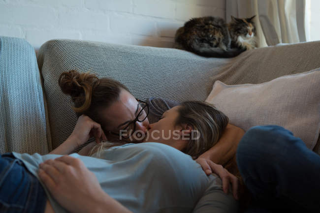 Lesbienne couple baisers sur canapé à la maison — Photo de stock