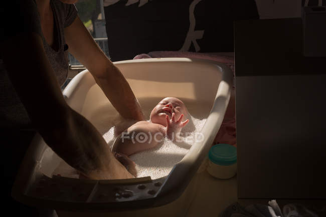 Mãe tomando banho seu bebê na banheira em casa — Fotografia de Stock