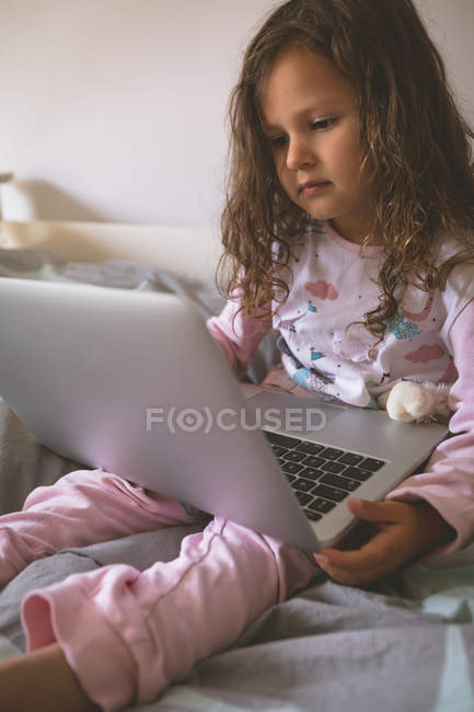 Primer plano de la chica que usa el ordenador portátil en la cama en el dormitorio en casa - foto de stock