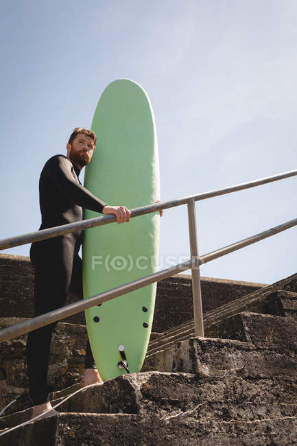 Surfer mit Surfbrett steht an einem sonnigen Tag auf der Treppe — Stockfoto