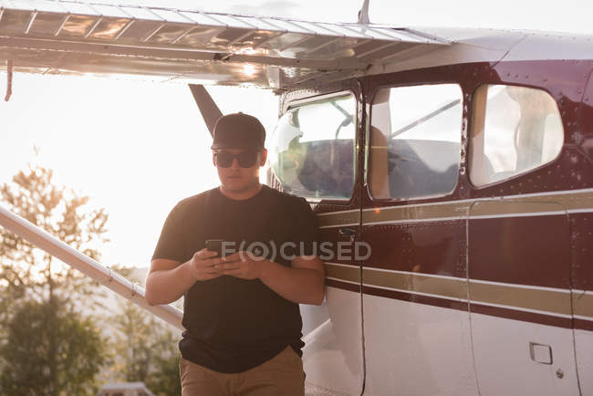Pilot using mobile phone near aircraft on sunny day — Stock Photo