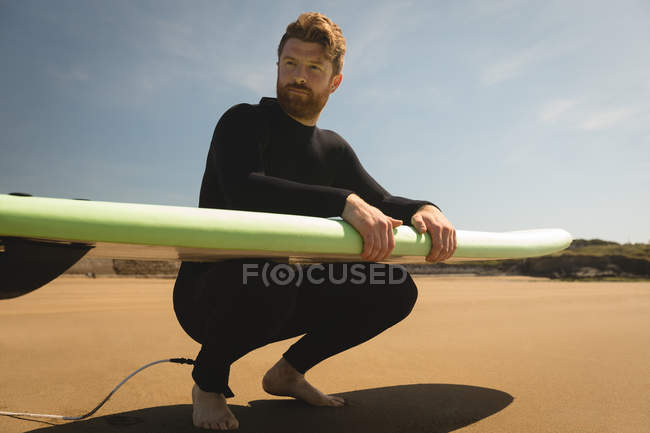 Surfeur avec planche de surf assis à la plage par une journée ensoleillée — Photo de stock