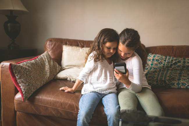 Les filles utilisant un téléphone mobile sur le canapé à la maison — Photo de stock