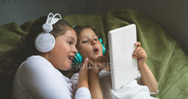 Frères et sœurs écoutant de la musique tout en utilisant une tablette numérique à la maison — Photo de stock