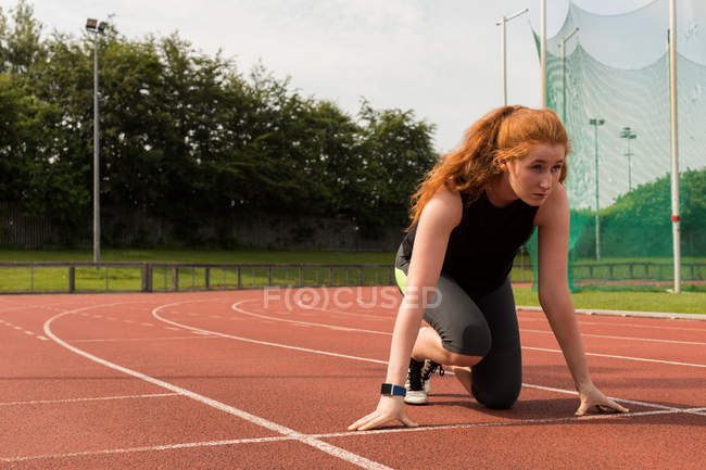 Jeune athlète féminine prête à courir sur piste de course — Photo de stock