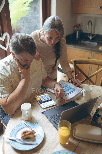 Старшая пара за цифровым планшетом на обеденном столе дома — стоковое фото