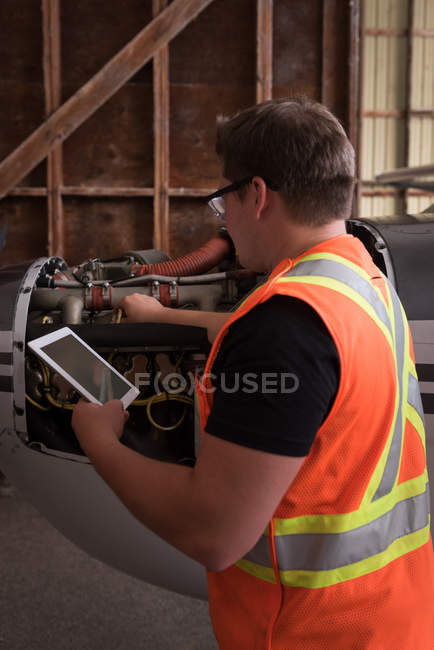 Mechanic using digital tablet while servicing aircraft engine at aerospace hangar — Stock Photo