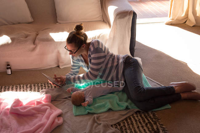 Мать с ребенком, используя цифровой планшет на полу дома — стоковое фото