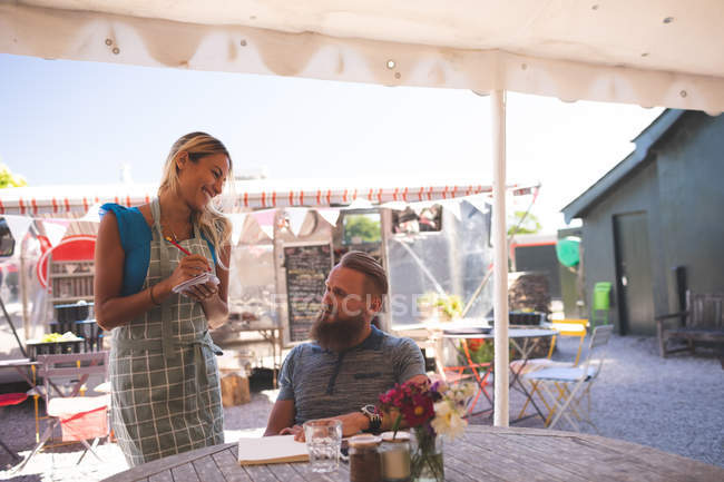 Жіноча офіціантка робить замовлення у відкритому кафе на сонячний день — стокове фото