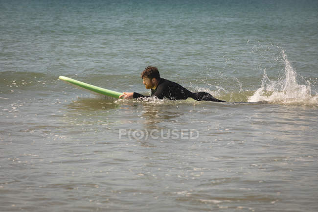 Vista lateral del surfista surfeando en agua de mar - foto de stock