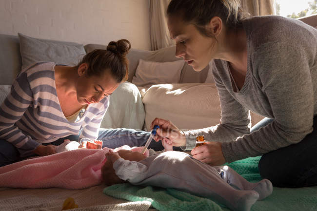 Lesbian couple feeding medicine to their babies at home — Stock Photo